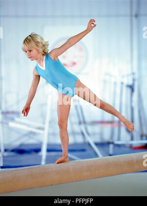 Blonde junge Turnerin in blau Body üben arabesque Position auf Strahl, Seitenansicht Stockfoto