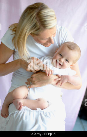 Babysitting auf Woman's Schoß, Frau Biegekopf und Baby, beide lachen Stockfoto