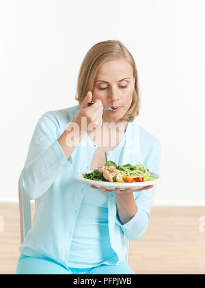 Frau sitzt auf Stuhl Essen Lachs Salat auf Hand ausgeglichen Stockfoto