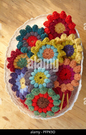 Bunte, gehäkelte Blumen im Korb, Holz Hintergrund Stockfoto