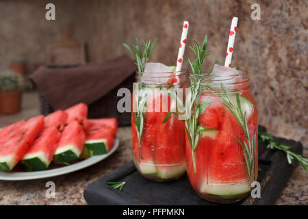 Zwei Gläser erfrischenden Sommerdrink mit Wassermelone und Rosmarin vor einem dunklen Hintergrund. Wassermelone und Rosmarin infundiert Wasser mit Eis. Konzept der Stockfoto