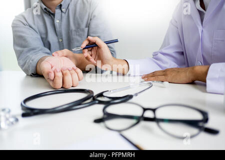 Attraktive männlicher Arzt Untersuchung über Berichte mit Massage Patient leidet unter Rückenschmerzen in Klinik Stockfoto