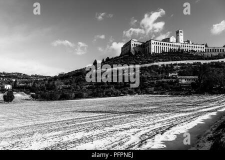 Blick auf die Stadt Assisi (Umbrien) im Winter, mit einem Feld durch Schnee und Himmel mit weißen Wolken bedeckt Stockfoto