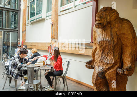 Besucher genießen Sie leichte Mittagessen im Innenhof, wo die aus Holz geschnitzte Sasquatch stand in der Ecke am Pike Place Market, Seattle, Washington, USA. Stockfoto