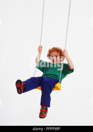 Ingwer schwarzhaarige Junge auf der Schaukel, lächelnd Stockfoto