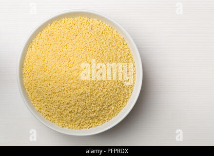Haufen rohe, ungekochte Couscous in weiße Schüssel Draufsicht von oben auf weißem Holz- Hintergrund Stockfoto