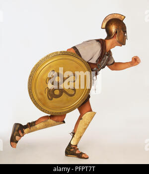 Mann mit Schirm gekleidet, wie griechische Krieger in Fahrstellung, Seitenansicht. Stockfoto