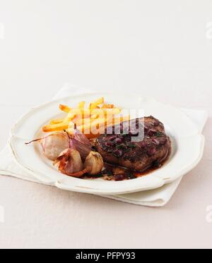 Minute Steak mit geröstetem Knoblauch, roten Zwiebeln und Pommes Frites, auf einer Platte Stockfoto