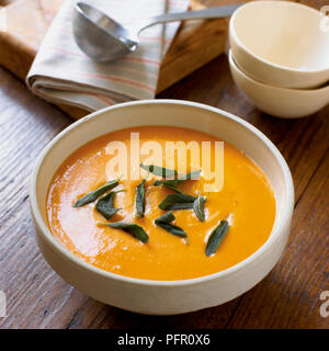 Kürbissuppe garniert mit Salbei in der Schüssel auf hölzernen Tisch serviert, close-up Stockfoto