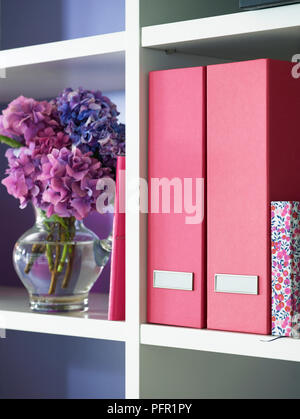 Rosa und floralen Muster Ring Binder und Vase mit rosa und lila Geranien auf Weiß Regal im Home Office, close-up Stockfoto