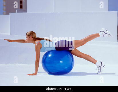 Liegende Frau auf Fitness Ball tun stretching Übung, den rechten Arm und das linke Bein in der Luft, Seitenansicht Stockfoto