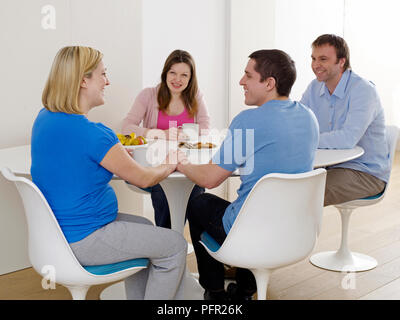 Gruppe von Freunden am Tisch sitzend diskutieren Arbeit mit schwangeren Frau und Mann Stockfoto