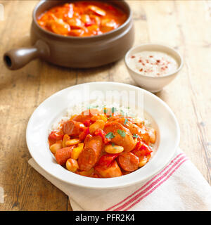 Wurstgulasch serviert mit weißer Reis in Weiß Schüssel und Klein Schüssel saure Sahne, close-up Stockfoto