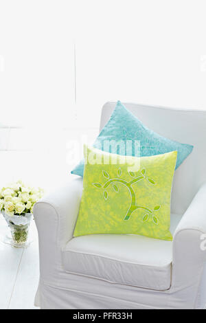 Sessel mit zwei Kissen auf, Bündel Rosen in einer Vase in der Nähe auf dem Boden Stockfoto