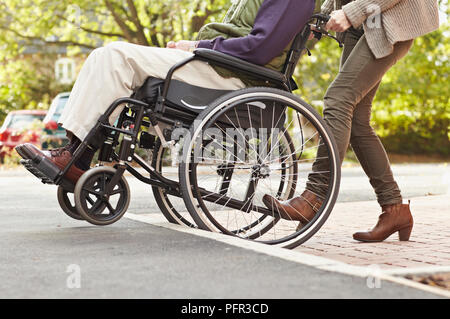 Frau drücken älterer Mann im Rollstuhl bis Schritt oder Auf-/Abfahrt auf Asphalt Stockfoto