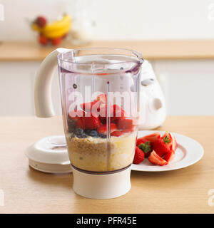 Milch, Brei Hafer, Blaubeeren und Erdbeeren in einen Mixer Stockfoto