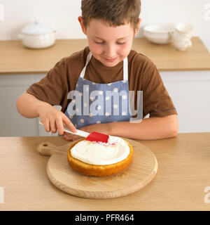 Junge Verbreitung Creme auf Biskuitboden mit einer Spachtel, 8 Jahre Stockfoto