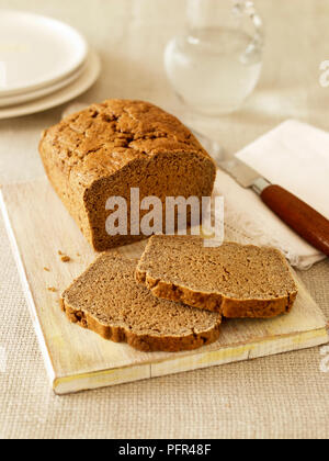 Glutenfreie basic braun Laib auf Schneidebrett mit zwei Scheiben Brot und Messer Stockfoto