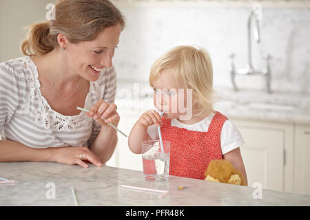 Kleines Mädchen (18 Monate) Trinken durch Stroh, Frau neben ihr sitzt, lächelnd Stockfoto
