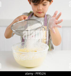 Junge Sichtung Mehl in eine Schüssel mit Kuchenteig, 7 Jahre Stockfoto