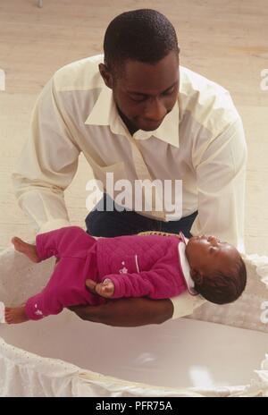 Mann Platzierung für 4 Wochen alten Baby Mädchen sorgfältig in Moses Korb Stockfoto