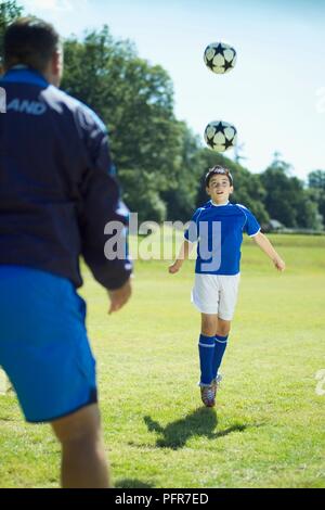 Junge Fußball-Spieler üben defensive Kopfzeilen, Trainer stehen in der Nähe Stockfoto