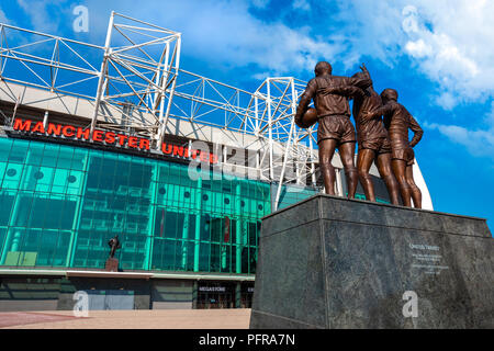 MANCHESTER, Großbritannien - 19 Mai 2018: Die United Trinity Bronze Skulptur, die mit George Best und Denis Law und Sir Bobby Charlton vor alten Tr aus Stockfoto