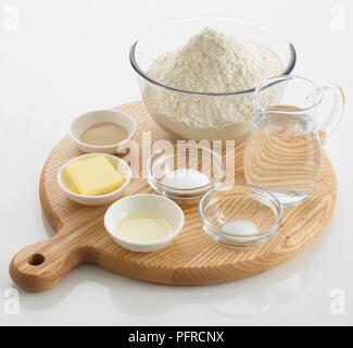 Erforderlichen Zutaten Brot, einschließlich Wasser, Mehl, Salz, Zucker, Butter, Hefe, in Schalen und einen Krug, auf einem Schneidebrett angeordnet Stockfoto
