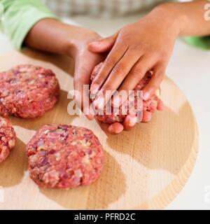 Das Mädchen Hände Abflachung Hackfleisch Mischung in Burger Form auf Schneidebrett, close-up Stockfoto