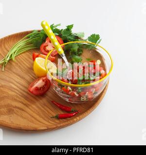 Tomaten, Koriander und Chili Salsa in Glas Schale mit Löffel, frische Stängel Koriander, in Scheiben geschnittene Tomaten, Zitrone, rote Chilis auf Schneidebrett Stockfoto