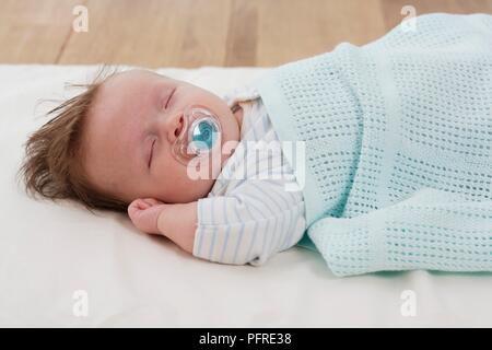 Baby Boy liegend mit Dummy in seinem Mund und bedeckt mit Baby Decke Stockfoto