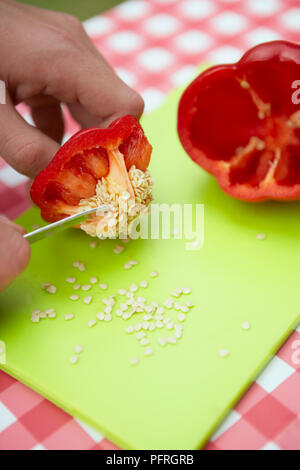 Frau mit kleine Küche Messer Samen von geschnittene rote Paprika auf Schneidebrett auf Picknick Tisch zu entfernen, close-up Stockfoto