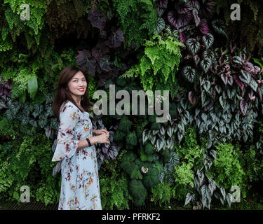 Porträt der schönen asiatischen Mädchen in geblümten Kleid vor der lebenden Pflanze Wand an Cloud Forrest der Garten an der Bucht von Singapur posieren. Stockfoto