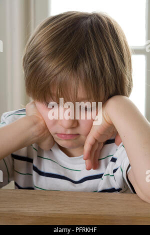 Junge sitzt am Tisch mit dem Kopf in seinen Händen Stockfoto