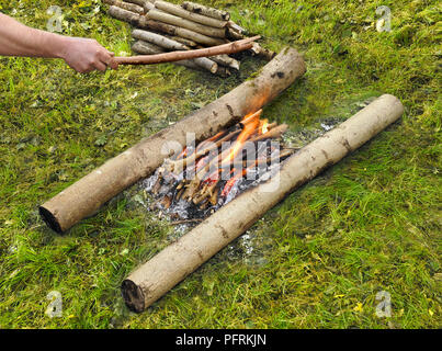 Mann mit Stock über dem Lagerfeuer in Flammen zwischen zwei Zweigen auf Gras Stockfoto