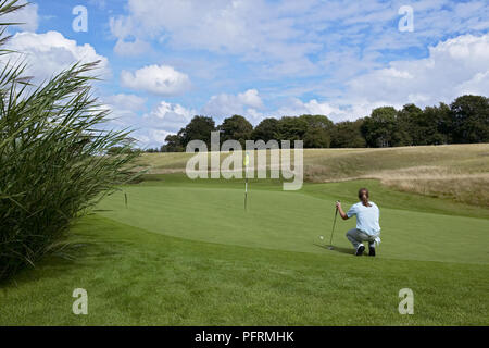 Weibliche Golfspieler hockend auf Putting Green, Golf Club, Ball in der Nähe im Gras Stockfoto
