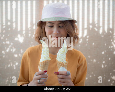 Schöne Frau kurze Haare tragen gelbe Shirt und Zwei Ton hat zwei Weiche dienen Vanilleeis Kegel auf Sommerzeit Stockfoto