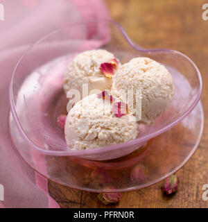 Herzförmigen rosa Glasschale mit drei Kugeln Rose und Vanilleeis garniert mit getrockneten Rosenblättern, close-up Stockfoto