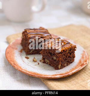Zwei Scheiben Toffee und Chocolate brownies auf rustikal anmutenden Steinzeug Platte auf Serviette, close-up Stockfoto
