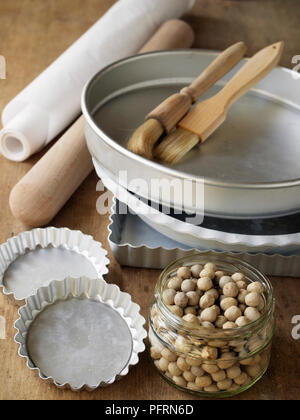Auswahl an Kuchen und Torte Dosen, Nudelholz, Backbohnen, Wachspapier, und basting Bürsten auf Holztisch, close-up Stockfoto