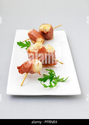 Spieß Jakobsmuscheln in Parmaschinken auf weißem Platter gewickelt Stockfoto