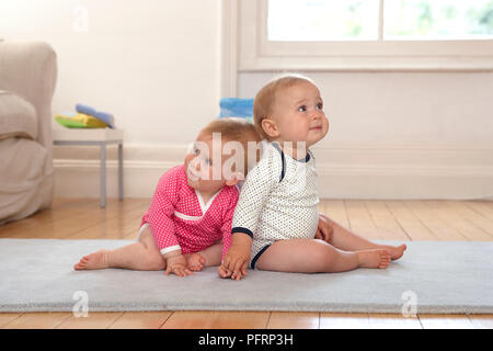 Twin Baby Mädchen und Jungen sitzen zusammen auf der Matte, 10 Monate Stockfoto