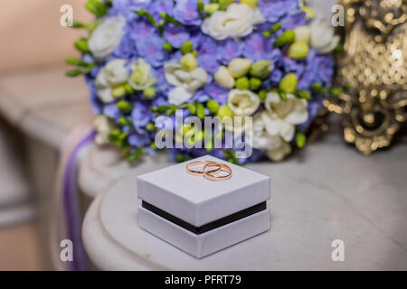 Trauringe liegen auf weißem Feld auf einen schönen Blumenstrauß Hintergrund, als Braut Zubehör. feierliche Veranstaltung, festliche Veranstaltung, Hochzeit, Tag. Paar goldene Ringe. Stockfoto