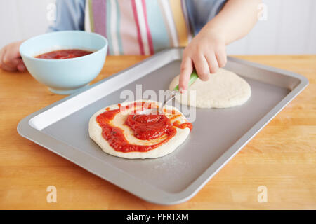 Junge Verbreitung Soße auf einer Pizza base Stockfoto