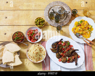 Marokkanisches Abendessen, einschließlich zahlouk (Auberginen dip) kesra (Brot), kesksou (Couscous), lahma meshwi (Lamm), Oliven, Pfefferminztee, salade d'Orangen a la Marocaine Stockfoto