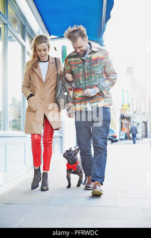 Junger Mann und Frau gehen Hund trägt eine rote Schleife binden sich in einer Straße. Stockfoto