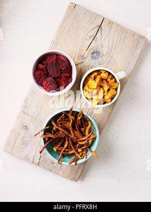 Gemüse-chips (Pastinake, Rote Beete, Süßkartoffel) in Schalen auf einem Holzbrett Stockfoto