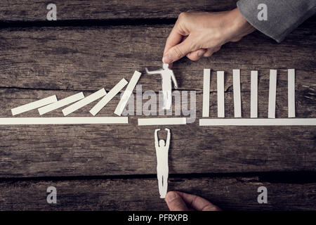 Zwei Geschäftsleute, die von Oben und Unten zur Unterstützung einer Papier Ausschnitt eines Mannes Stoppen der Domino Effekt. Stockfoto