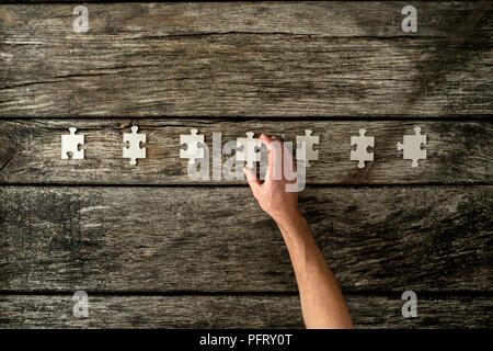 Top view of male hand placing seven blank puzzle pieces in a row on textured wooden boards. Stockfoto