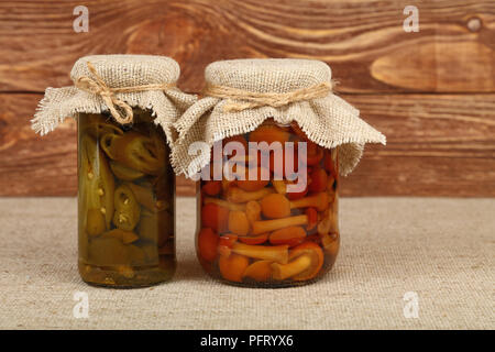 In der Nähe von zwei Gläsern Eingelegte grüne Hot jalapeno chili peppers und braun Honig Pilz Pilze mit Leinwand top Dekoration und Garn tabellec Stockfoto